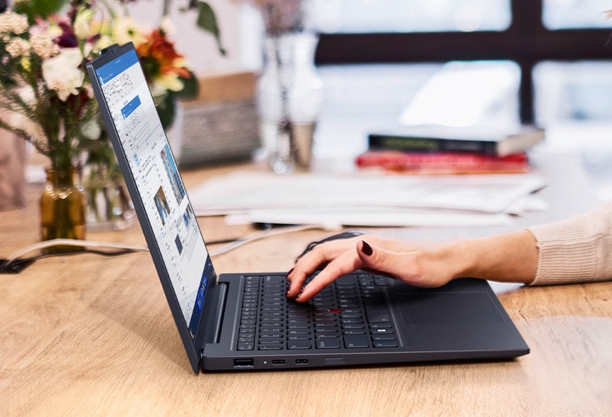 Cropped overhead shot of a person on a train using the Lenovo ThinkPad X1 Carbon Gen 12 laptop, on a table.