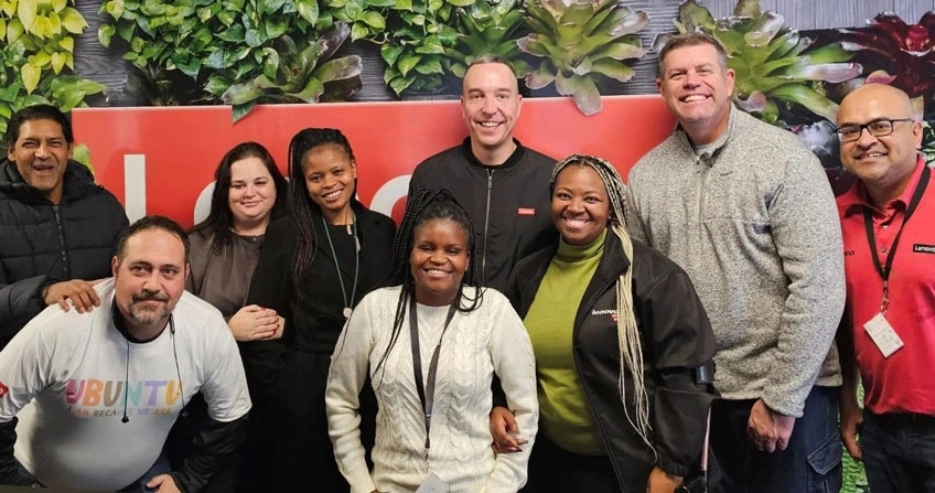 A diverse group of eight people smiling in front of a Lenovo sign