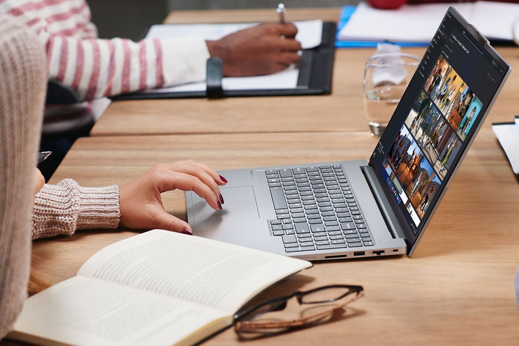 Cropped photo of the right-side profile of Lenovo ThinkBook in use on a desktop, along side eye glasses & an open book.